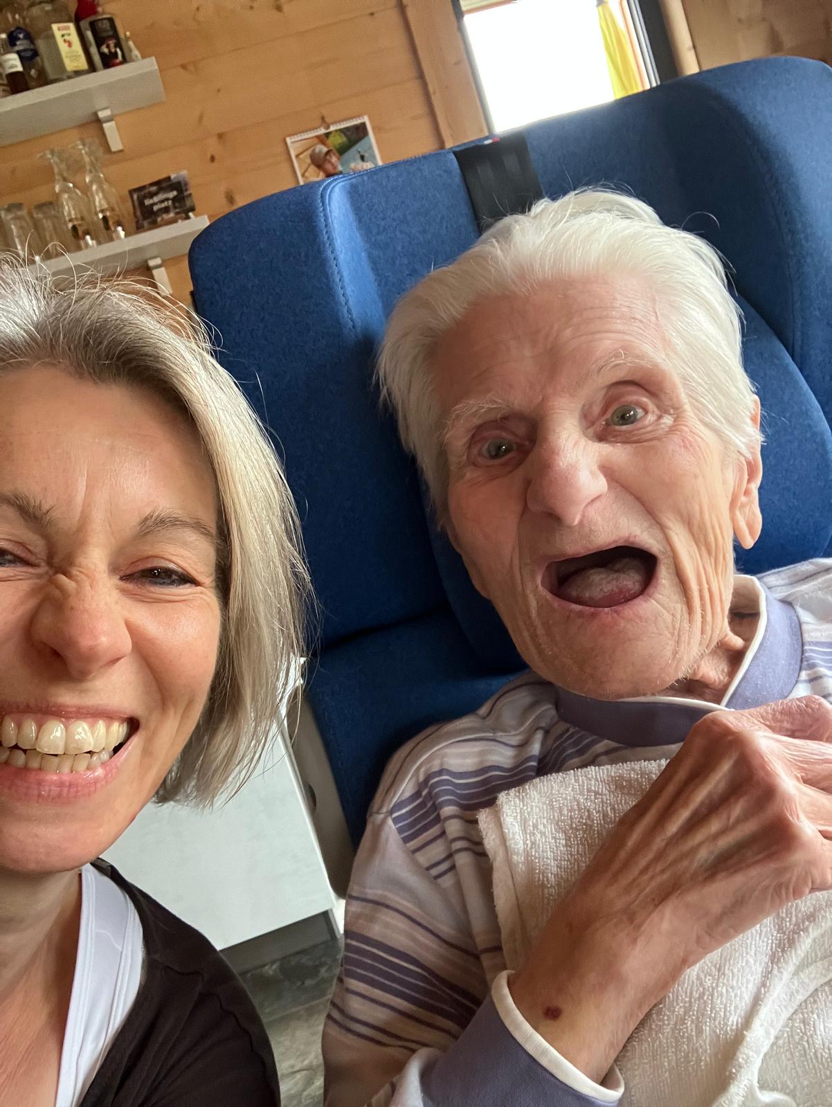 Betreuungskraft umarmt lächelnde Seniorin im Rollstuhl in einer hellen Küche